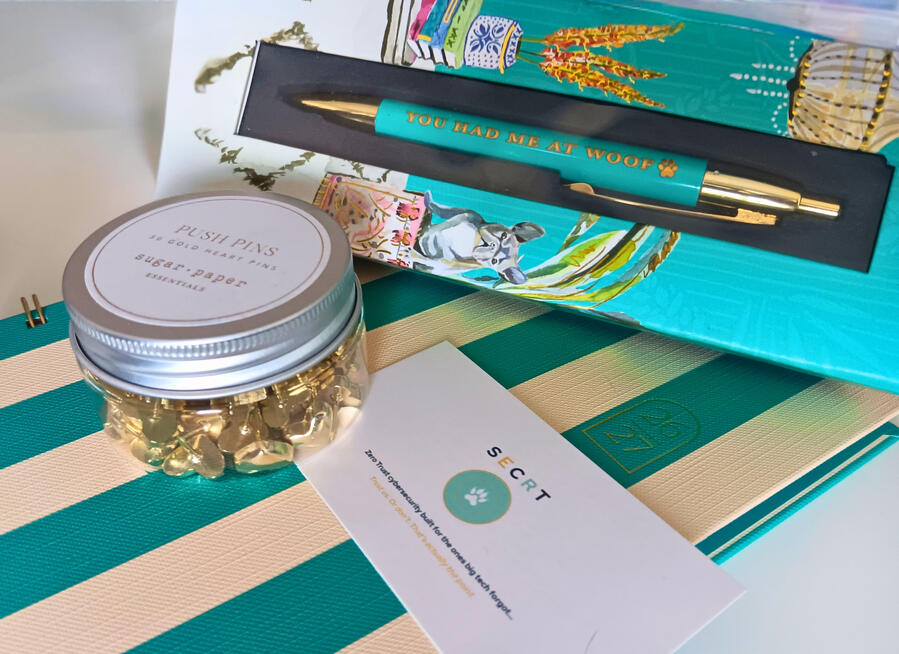 SECRT LLC business card displayed alongside gold push pins, a teal and gold pen, and a notebook on a striped surface.